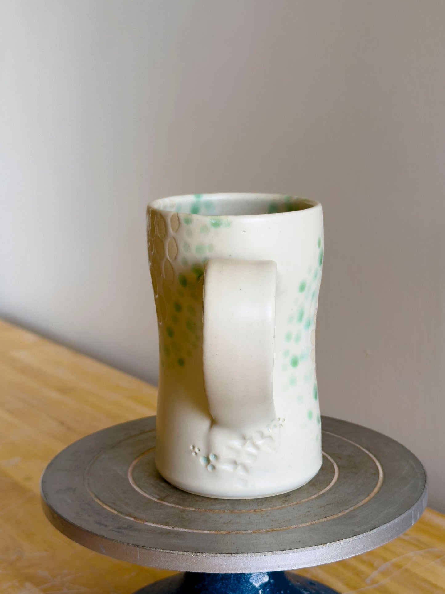 White ceramic mug with green speckles on a gray stand against a plain background