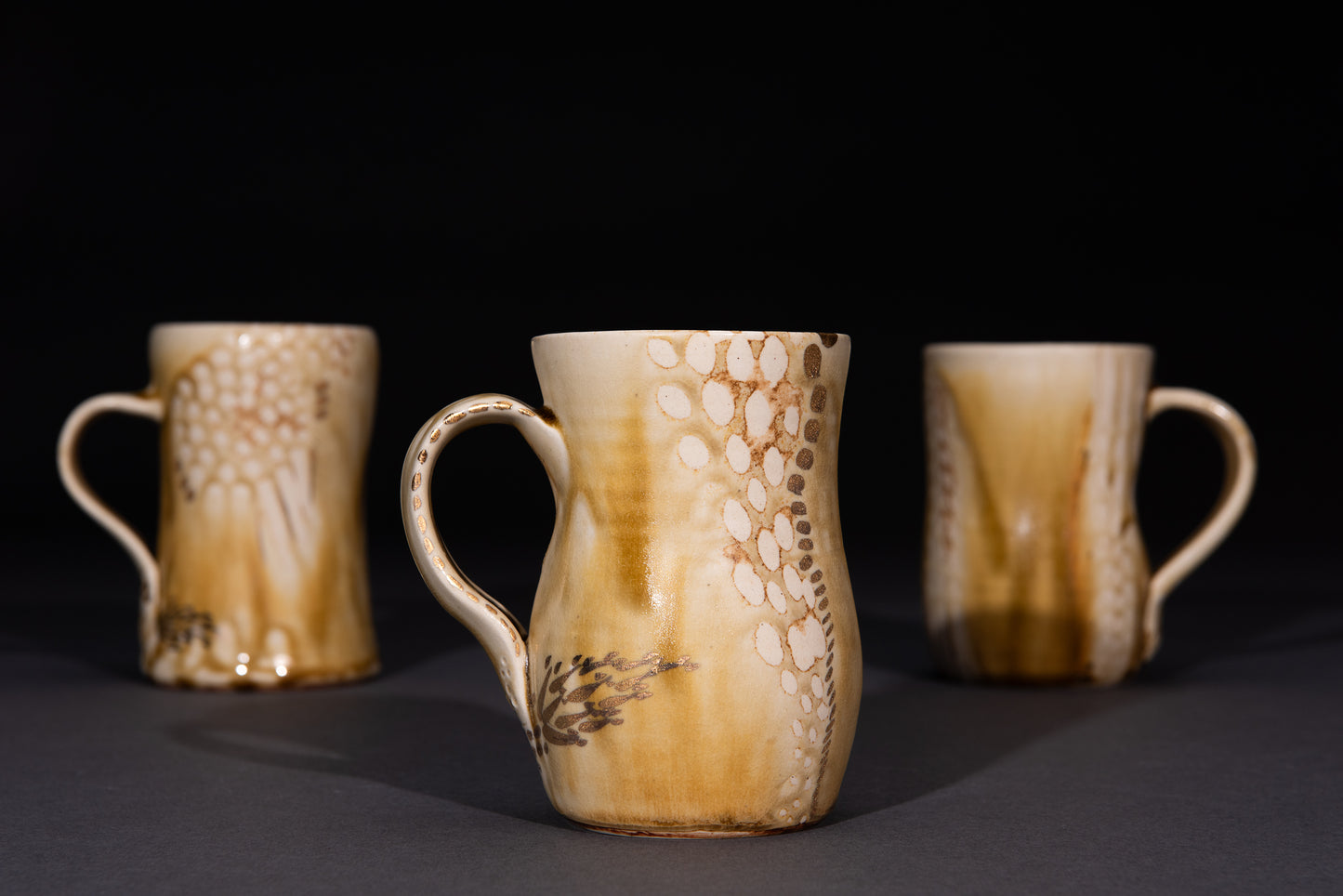 Three ceramic mugs with brown and beige patterns on a dark background