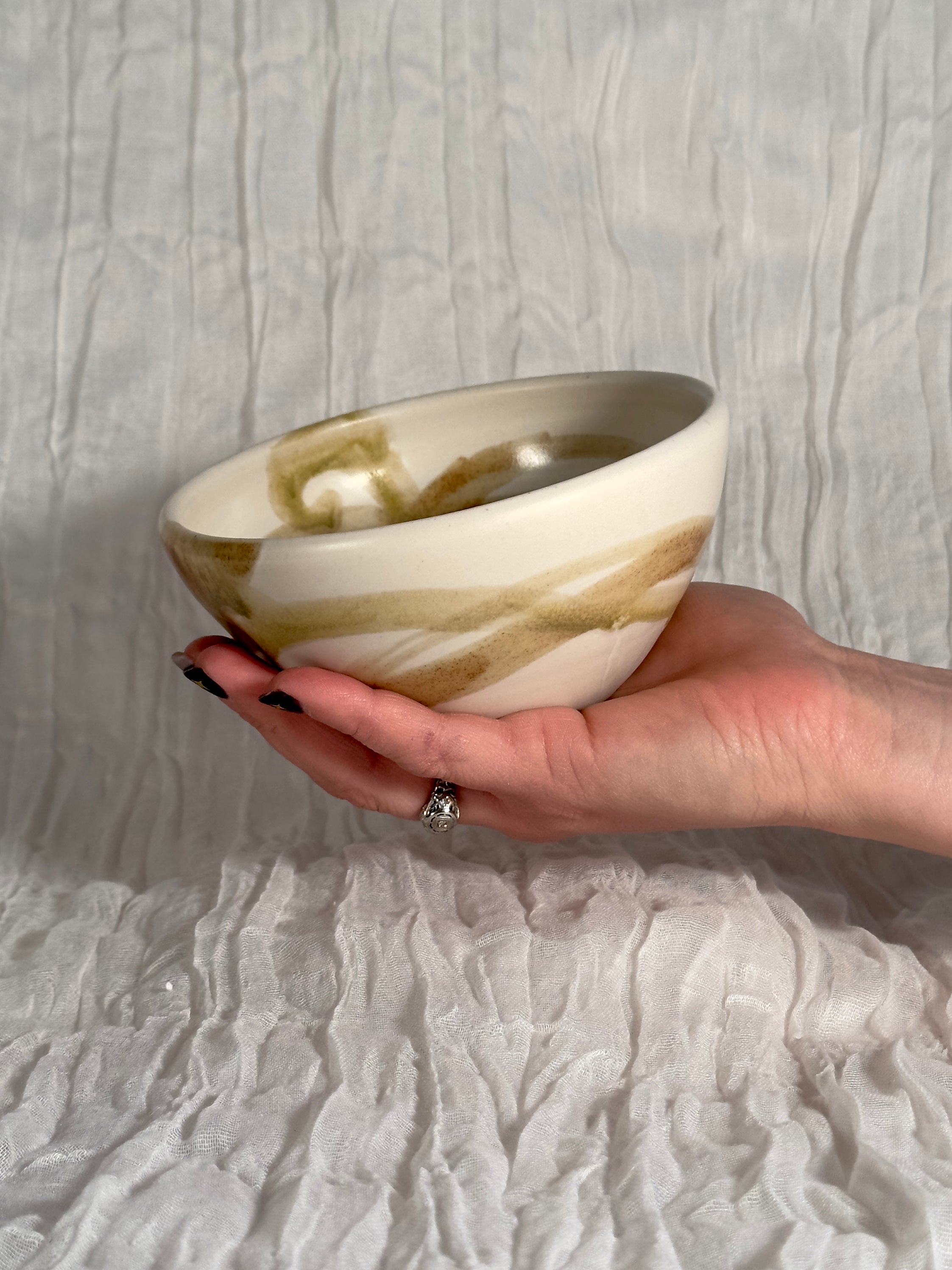 Hand holding a ceramic bowl with brown and beige swirl pattern against a textured gray background