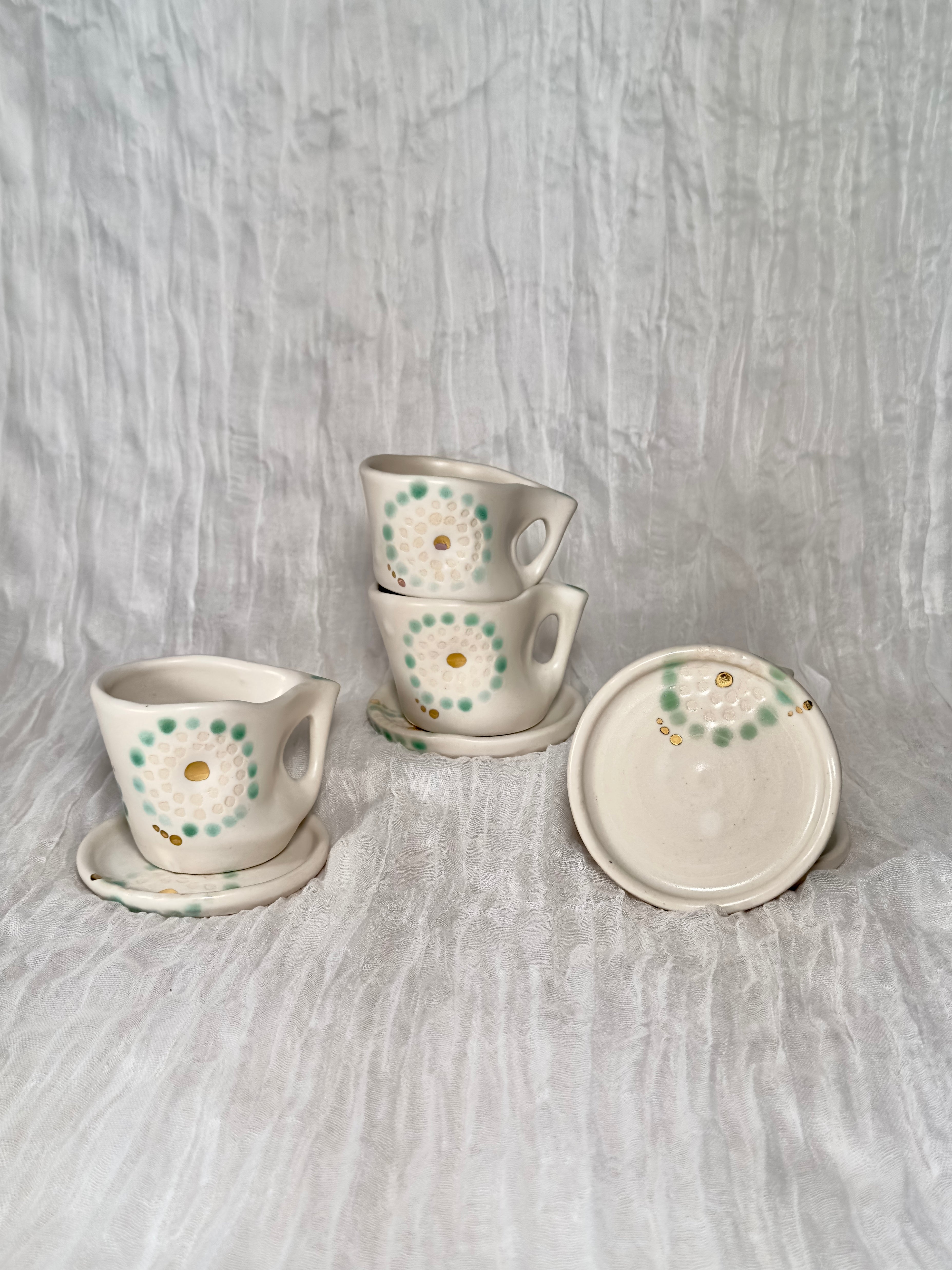 Set of ceramic cups and saucers with radiating dot patterns on a textured gray surface