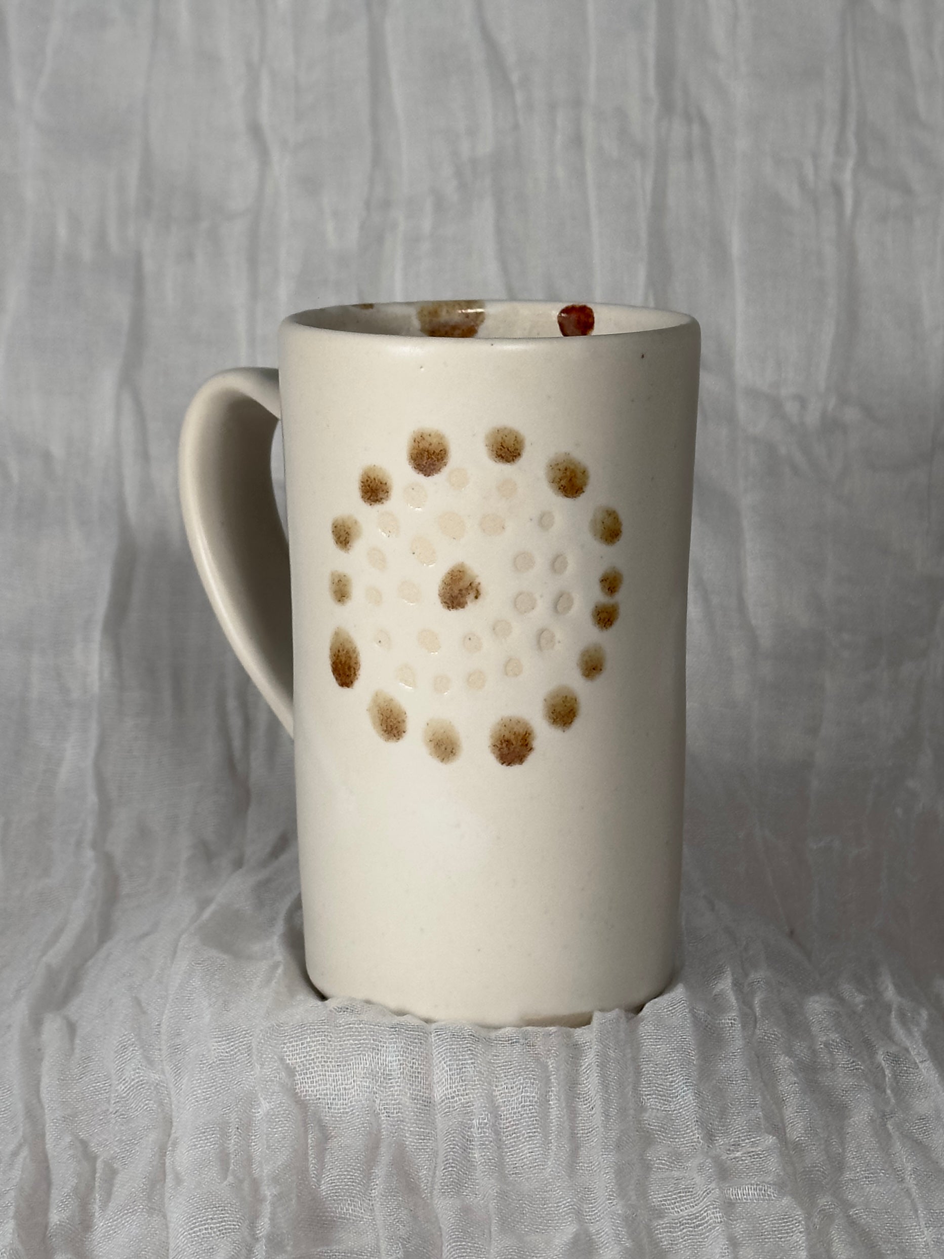 White ceramic mug with brown dot pattern on a gray textured background
