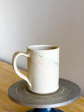 White ceramic mug on a small round wooden table against a plain wall.