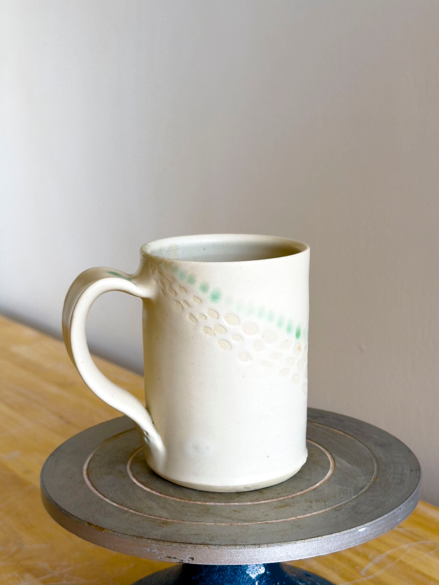 White ceramic mug on a small round wooden table against a plain wall.