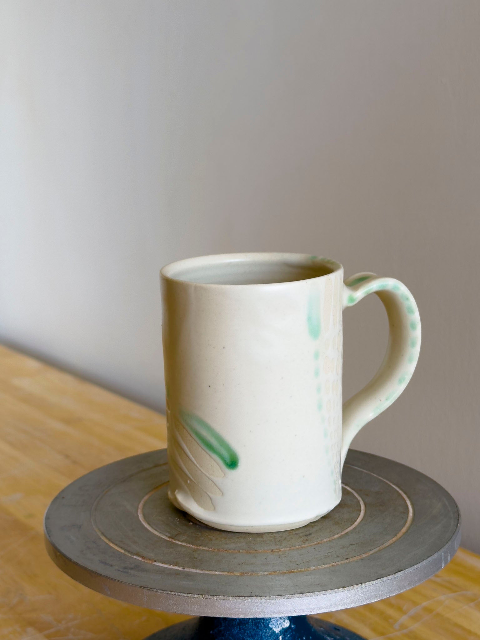 White ceramic mug with green accents on a small round table against a plain wall.