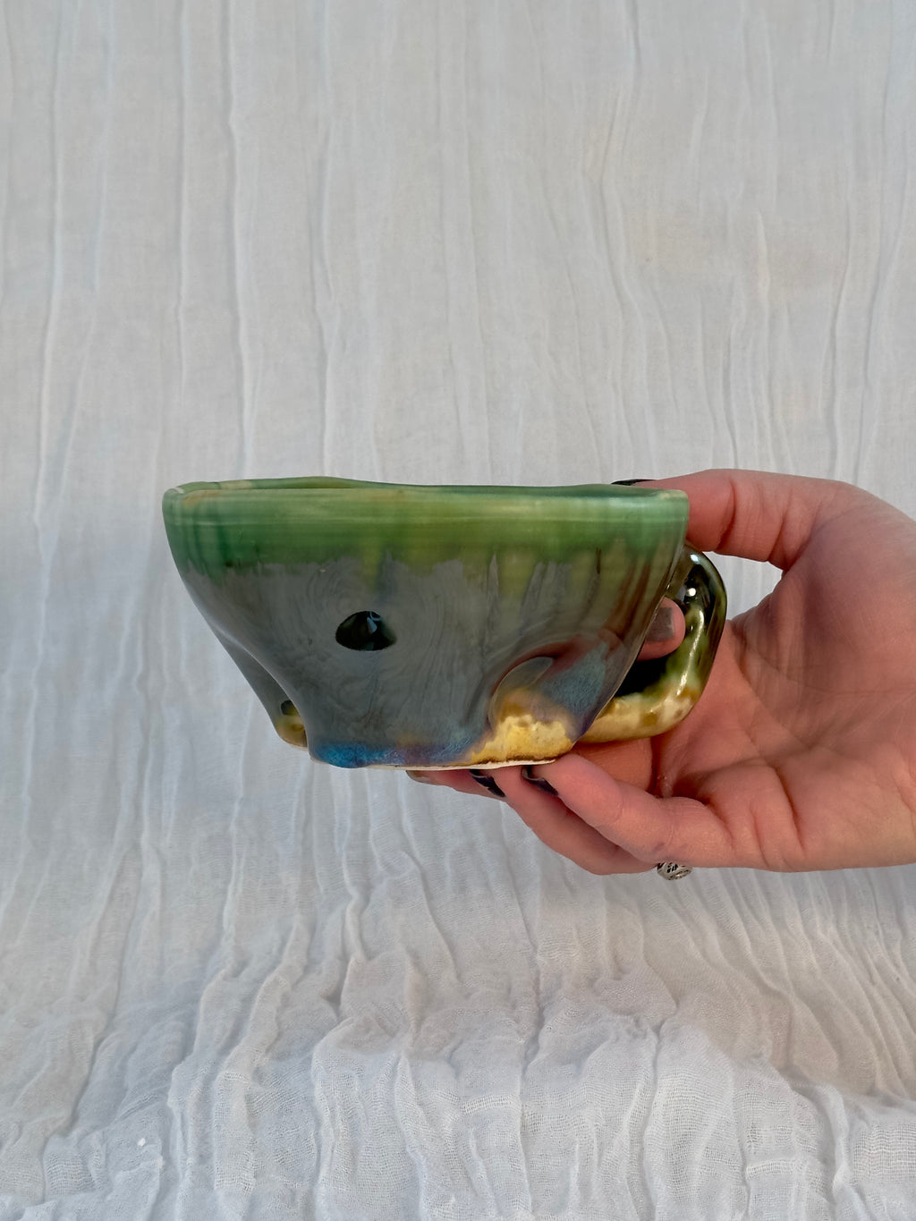 Hand holding a ceramic pot with a gradient finish on a white background
