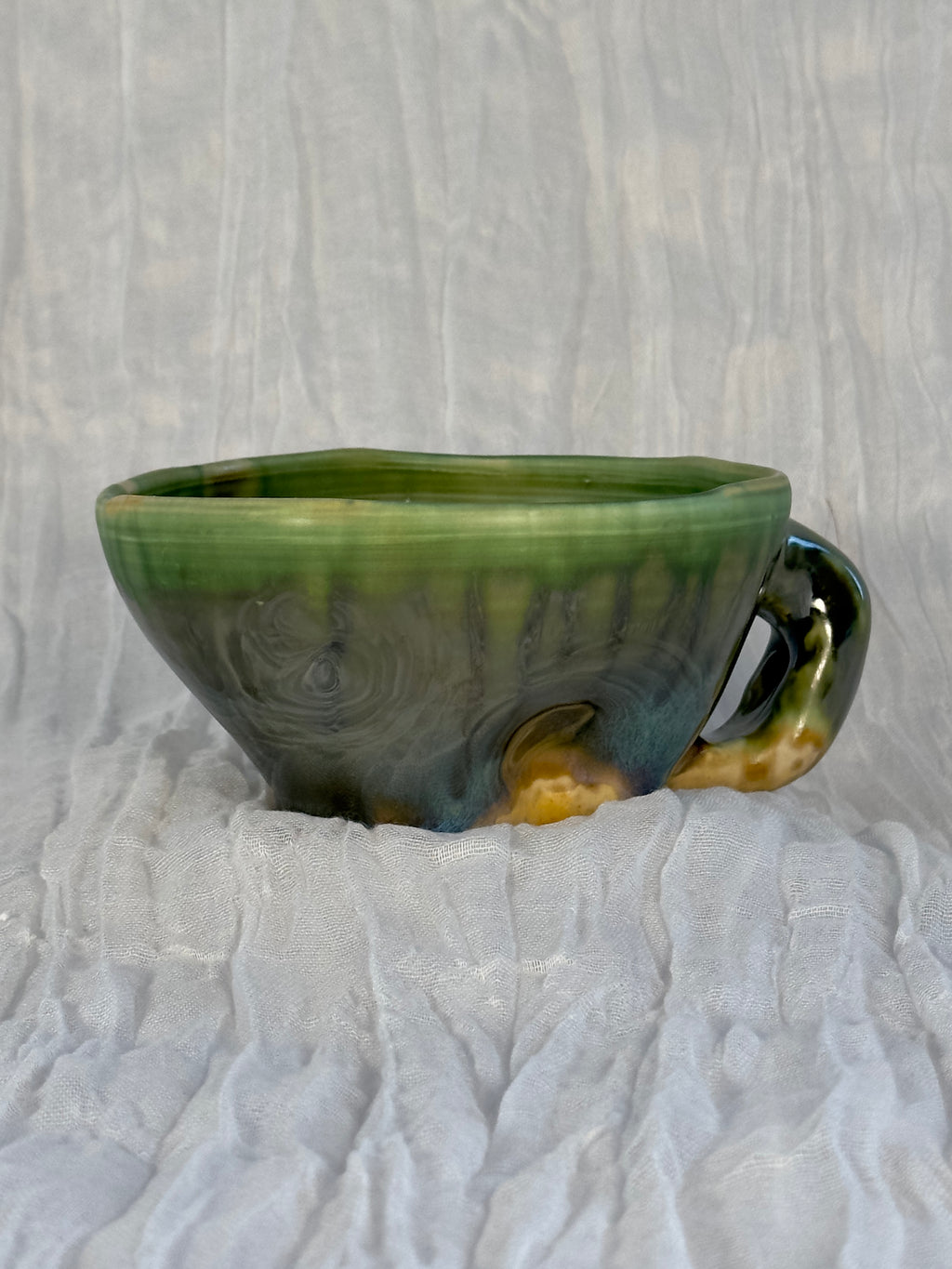 Green ceramic cup with a handle on a textured white surface