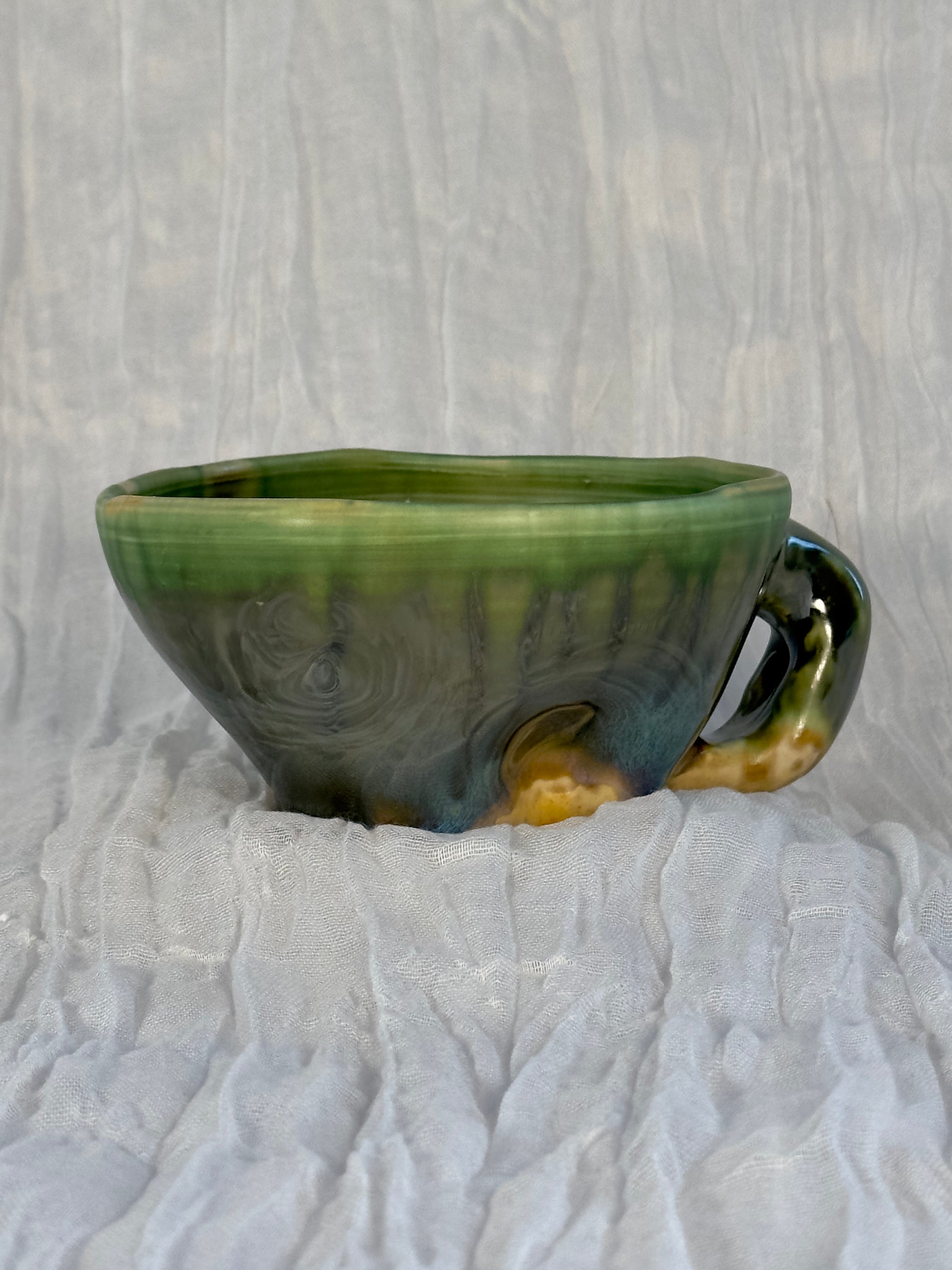 Green ceramic cup with a handle on a textured white surface