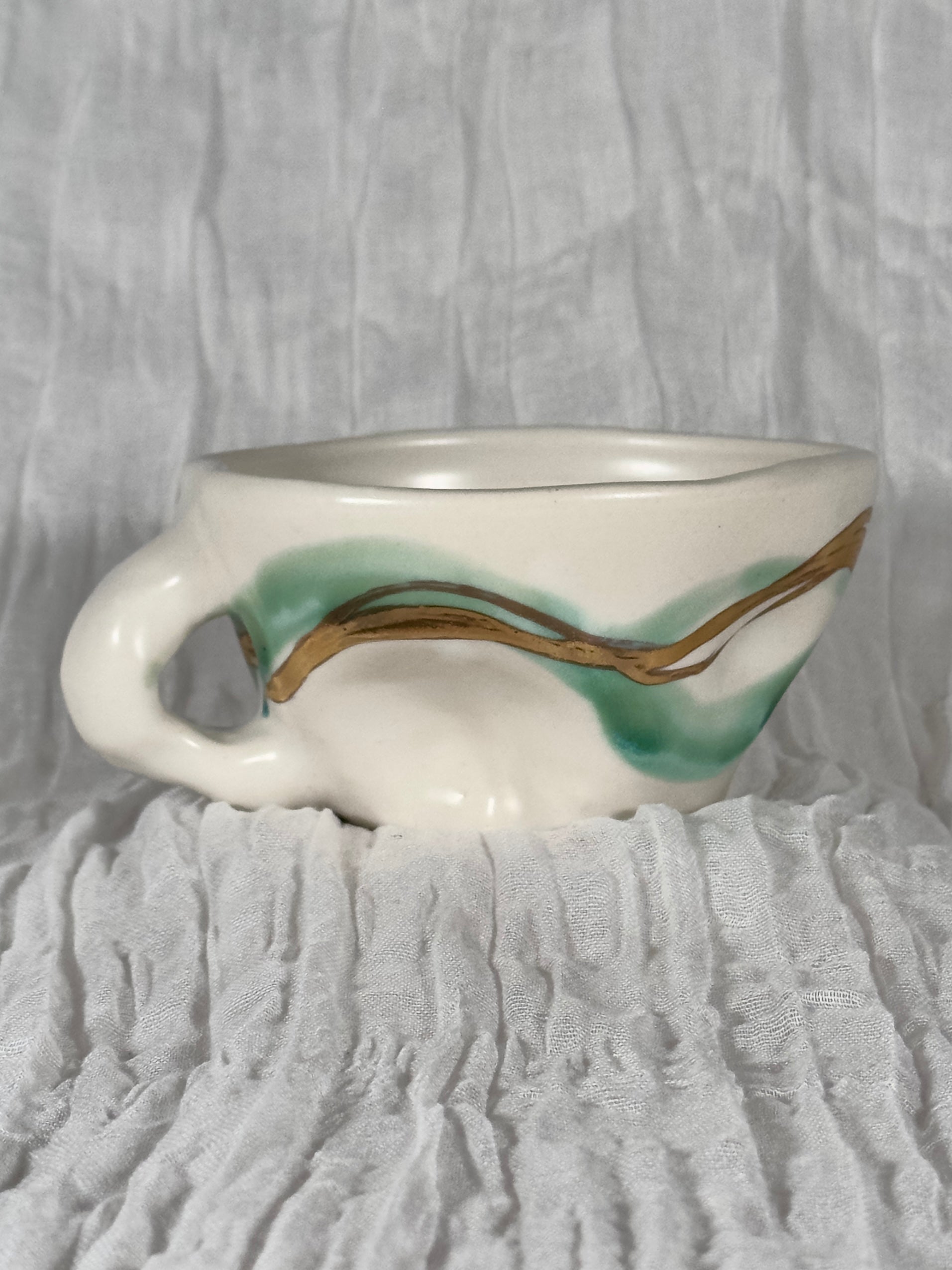 White ceramic cup with green and gold design on a textured gray background