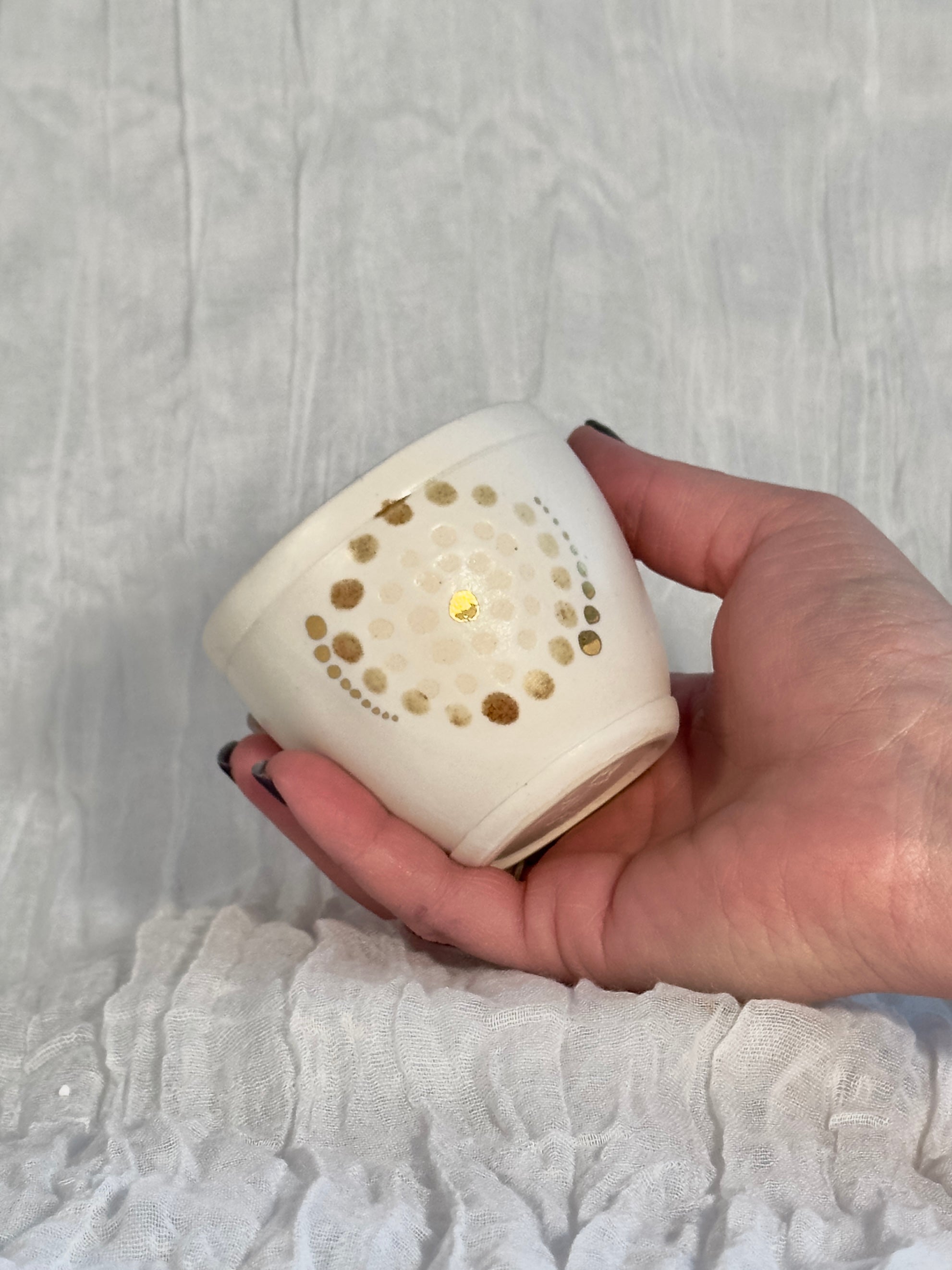 Hand holding a small white device with gold accents on a textured white background