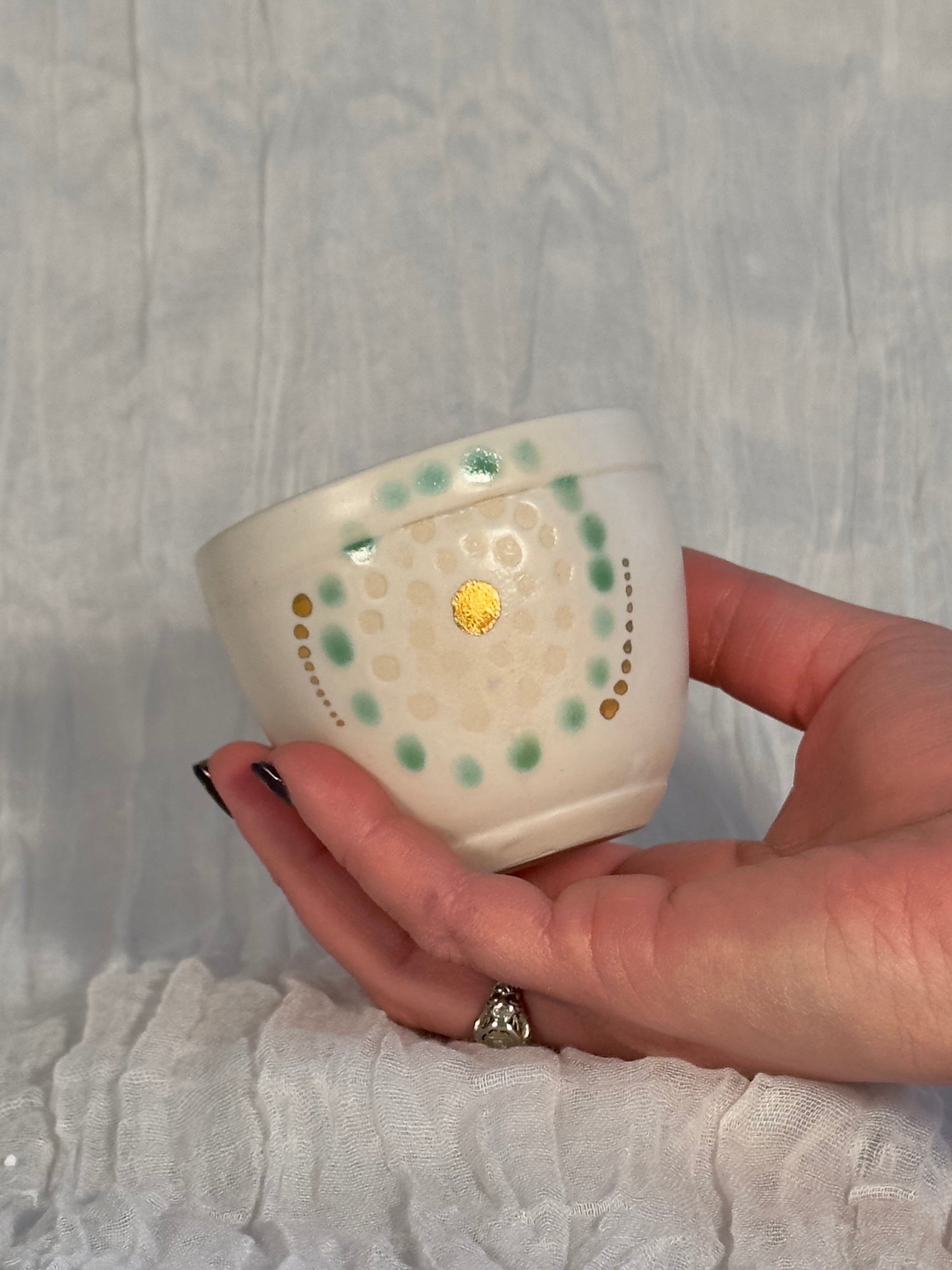 Hand holding a small ceramic cup with decorative patterns against a textured gray background