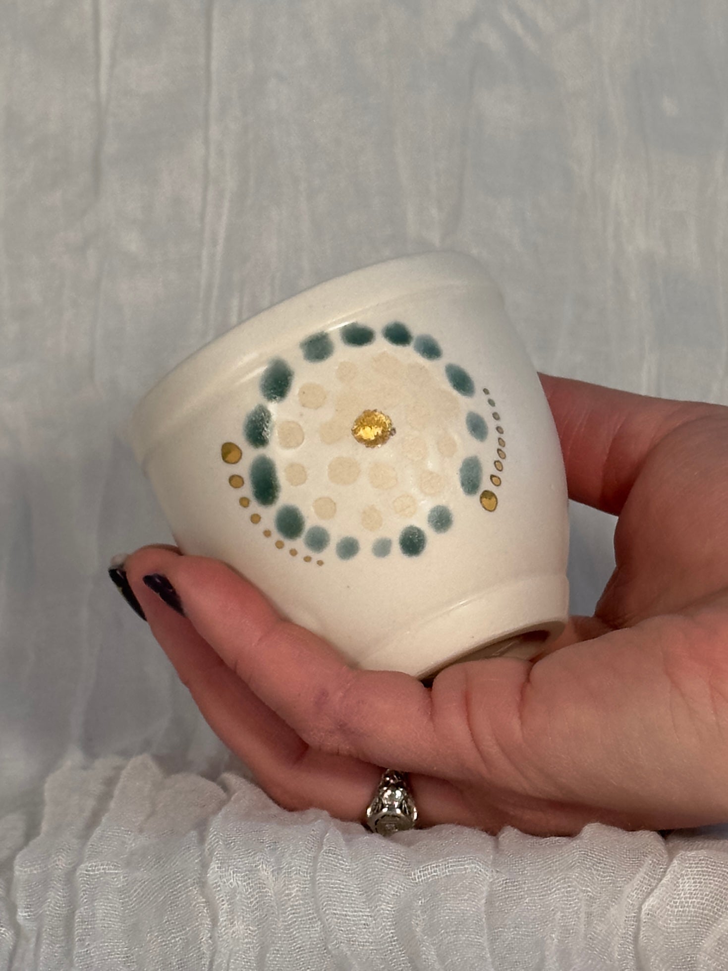 Hand holding a small ceramic container with decorative patterns against a light background