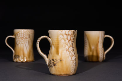 Three ceramic mugs with brown and beige patterns on a dark background