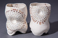 A sculptural ceramic drinking vessel with an organic, uneven form, featuring text saying "Who must I become?" and dot patterns.