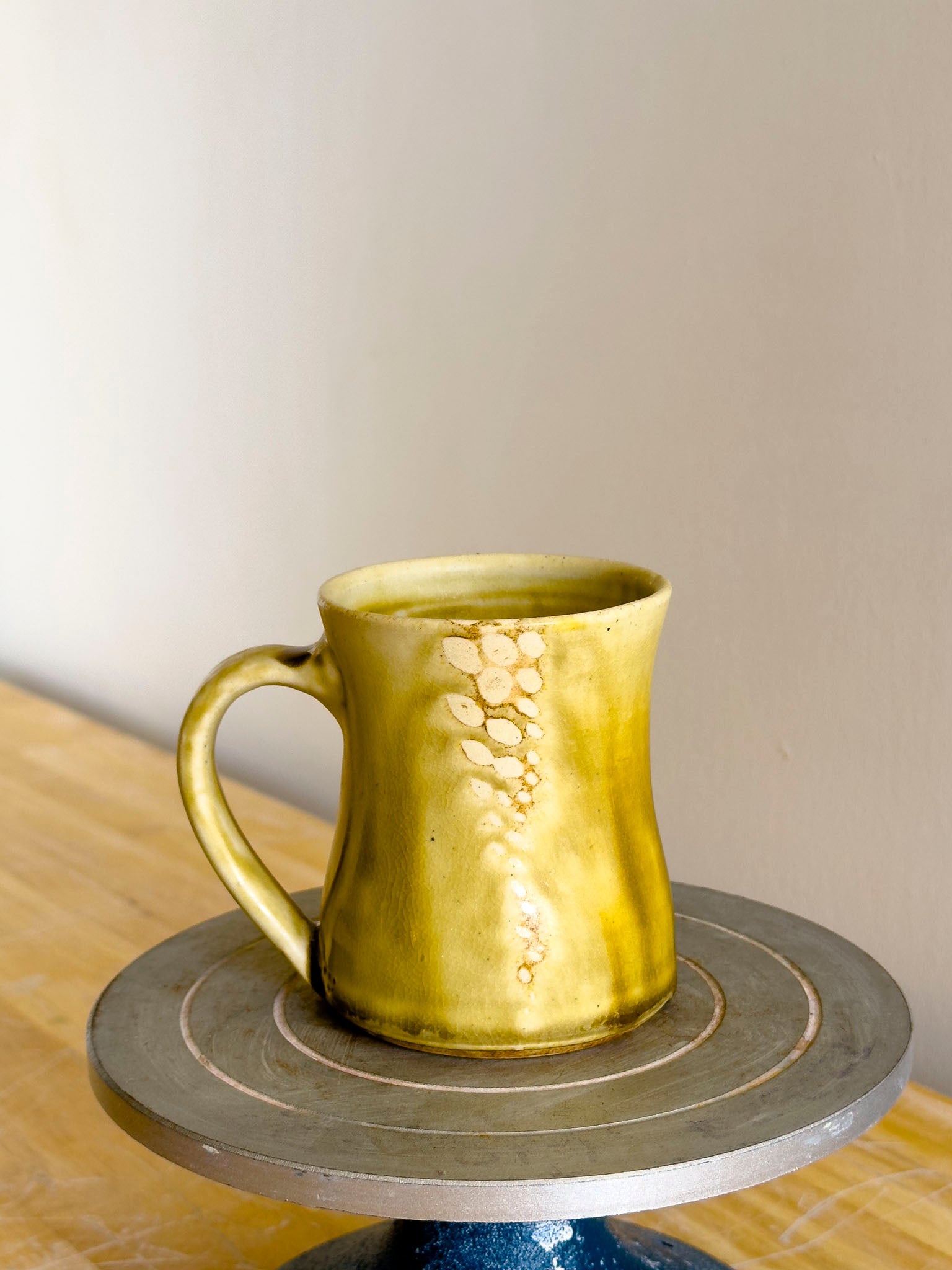Green ceramic mug on a pottery wheel with a neutral background