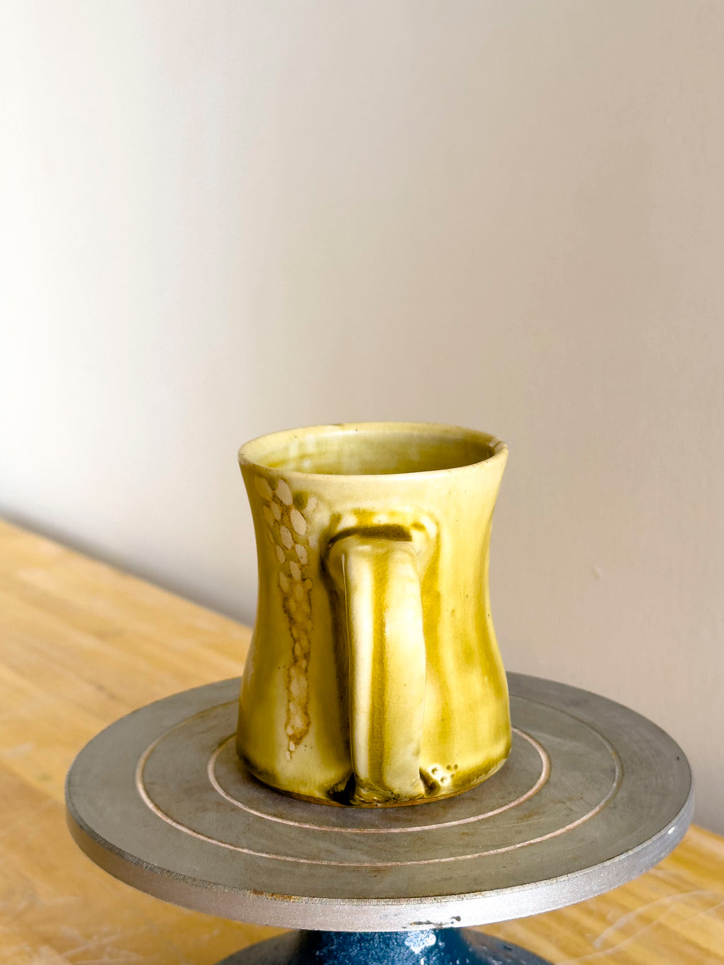 Yellow ceramic mug on a pottery wheel with a plain background