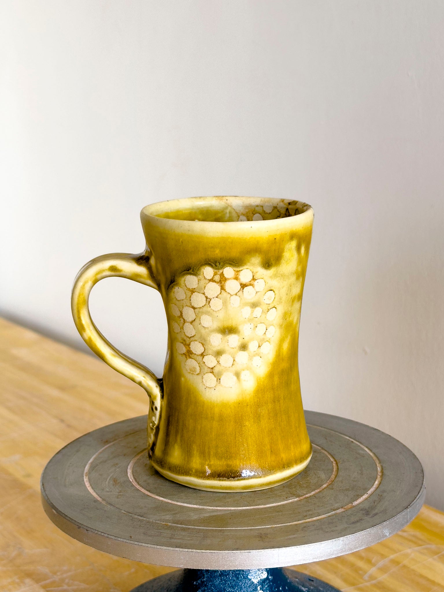 Yellow ceramic mug on a spinning wheel with a plain background