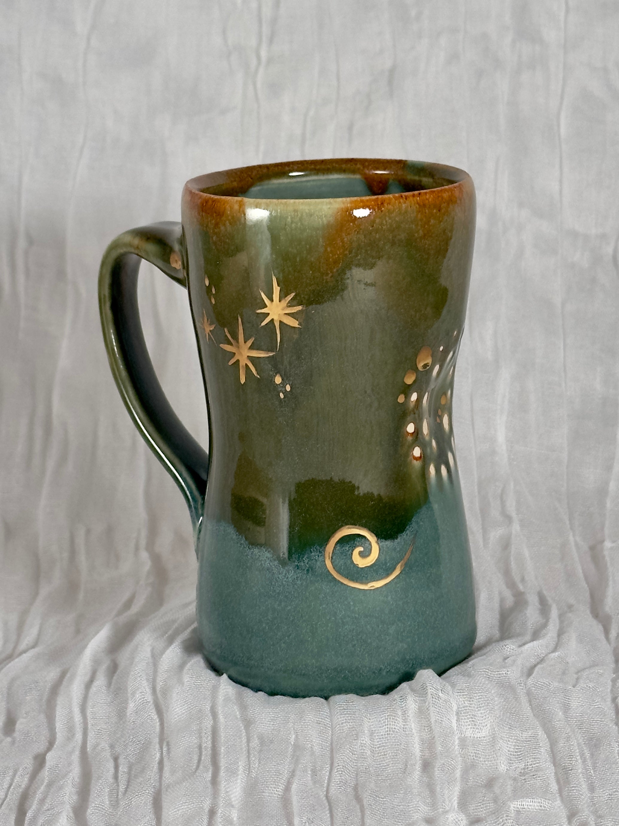 Green ceramic mug with star and circle designs on a textured gray background