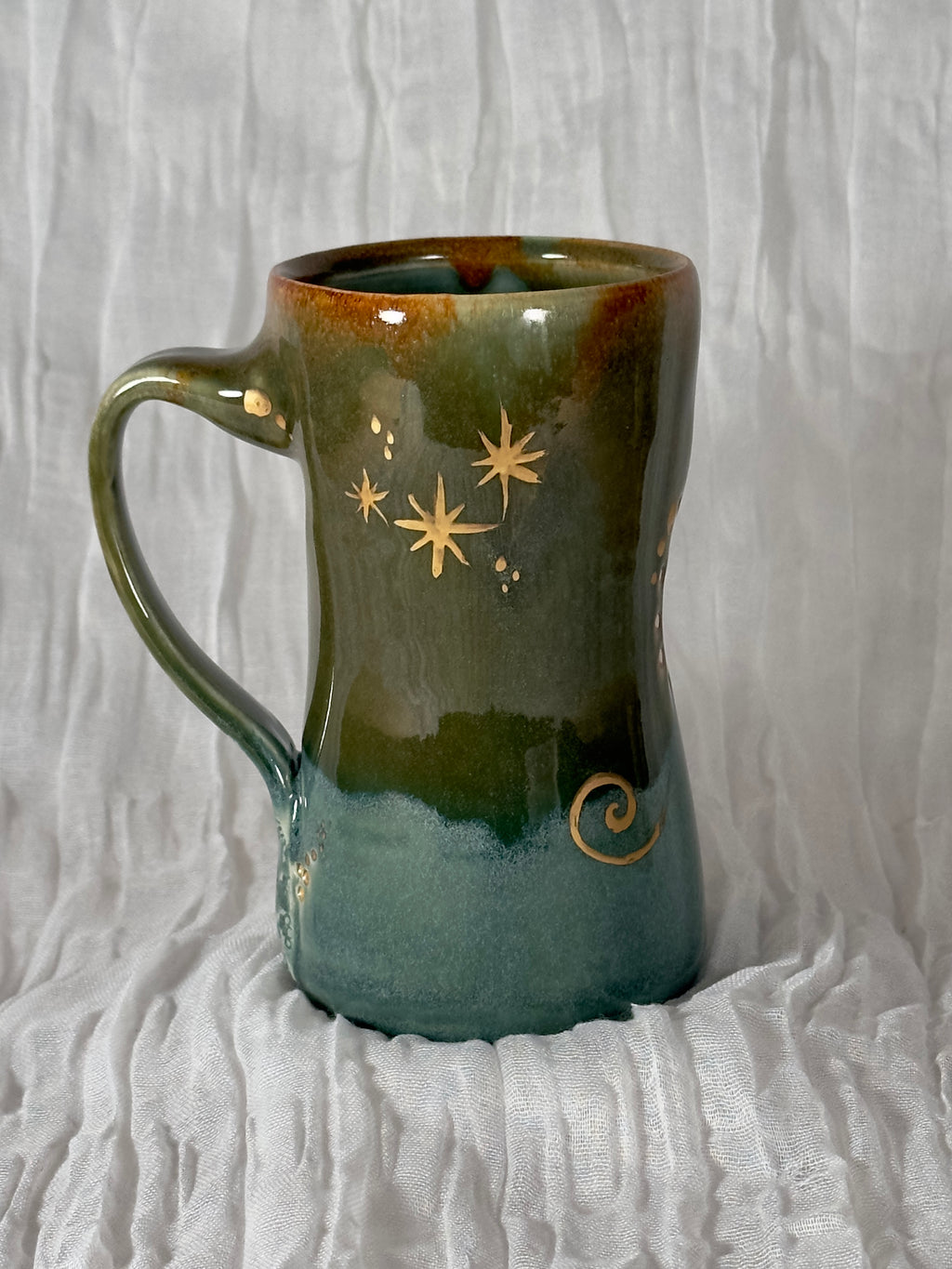 Green ceramic mug with star and swirl designs on a textured white background