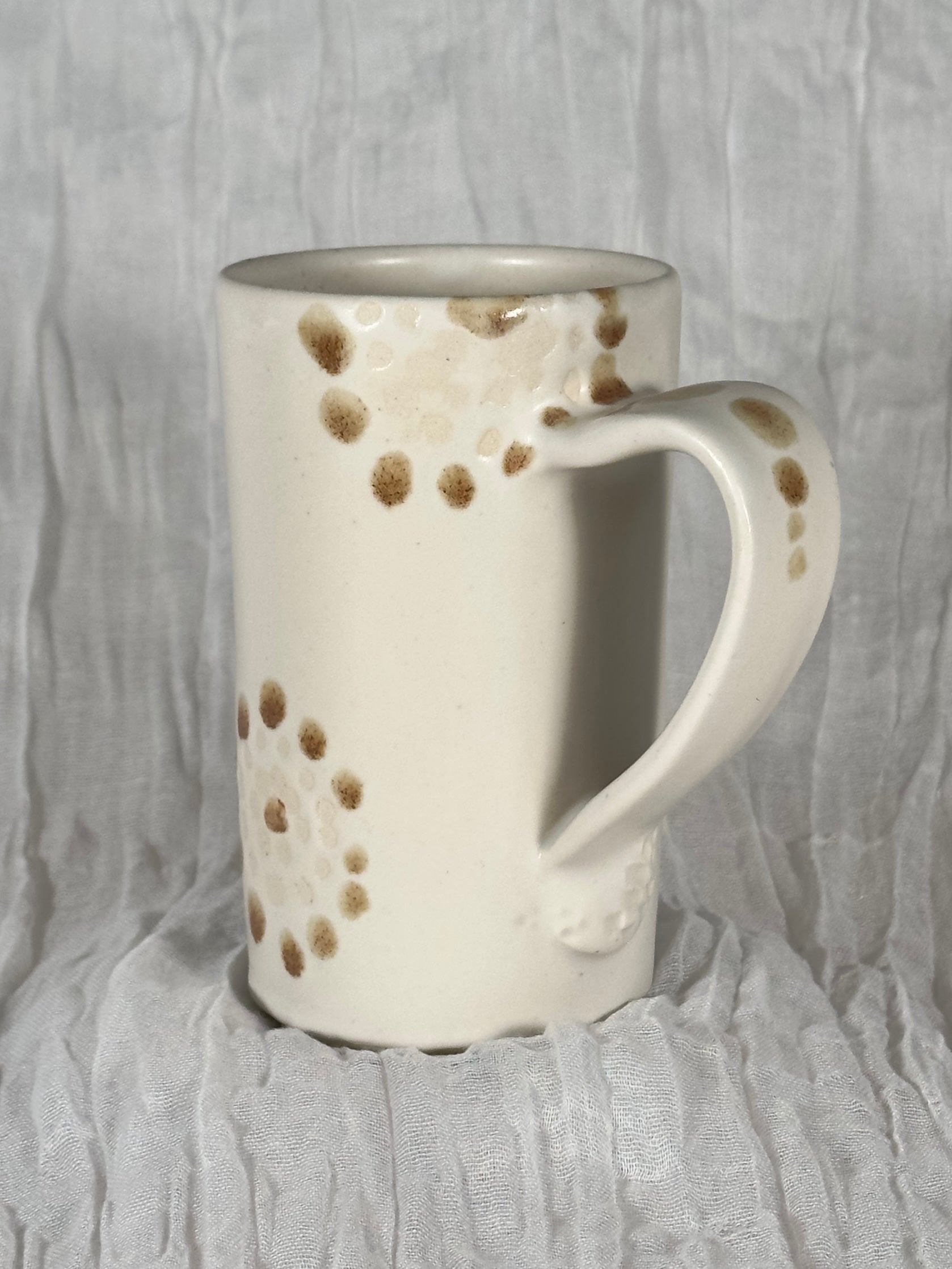 White ceramic mug with brown speckles on a textured gray background