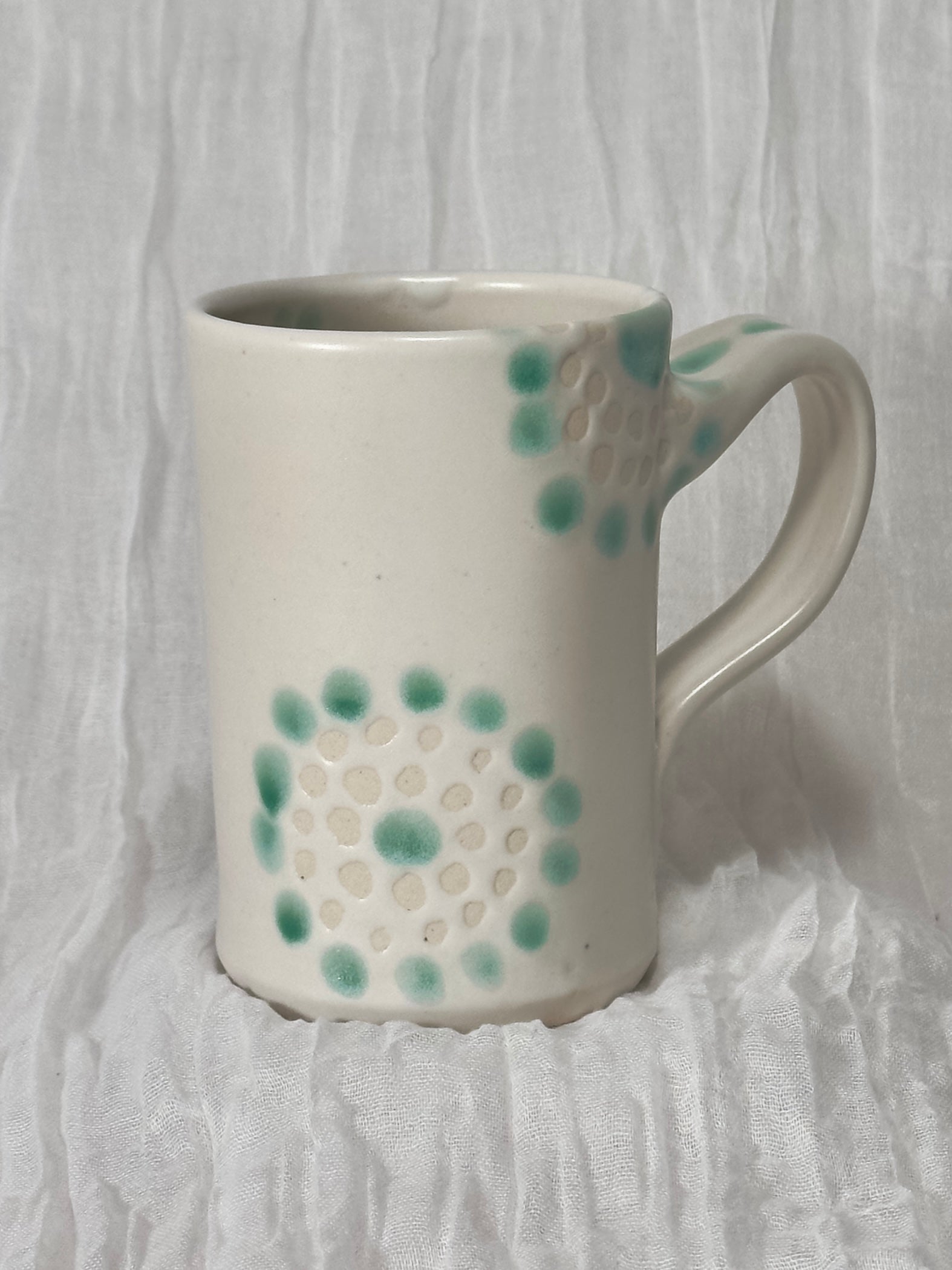 White ceramic mug with green floral pattern on a white textured background