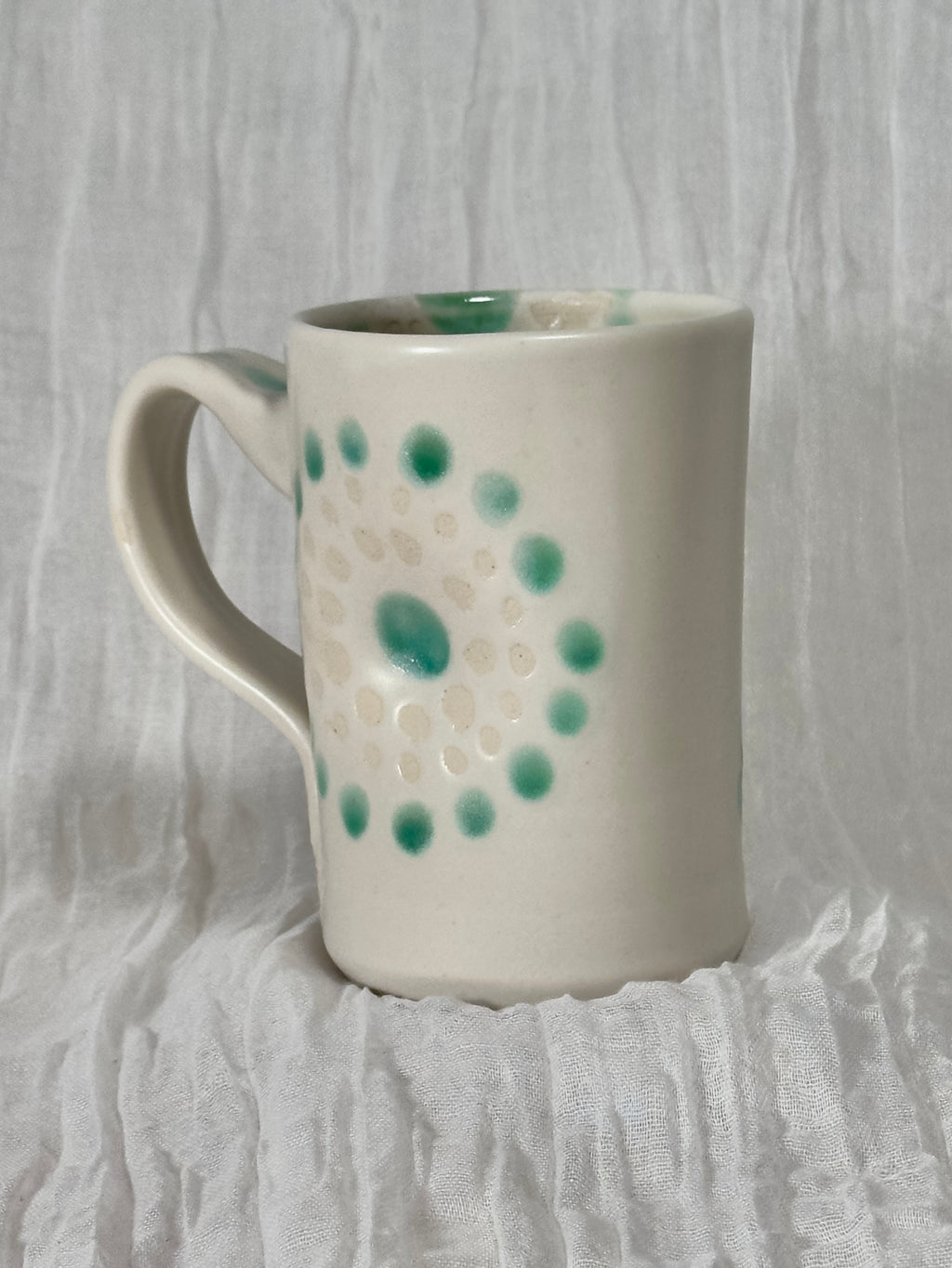 White ceramic mug with green speckles on a textured white background