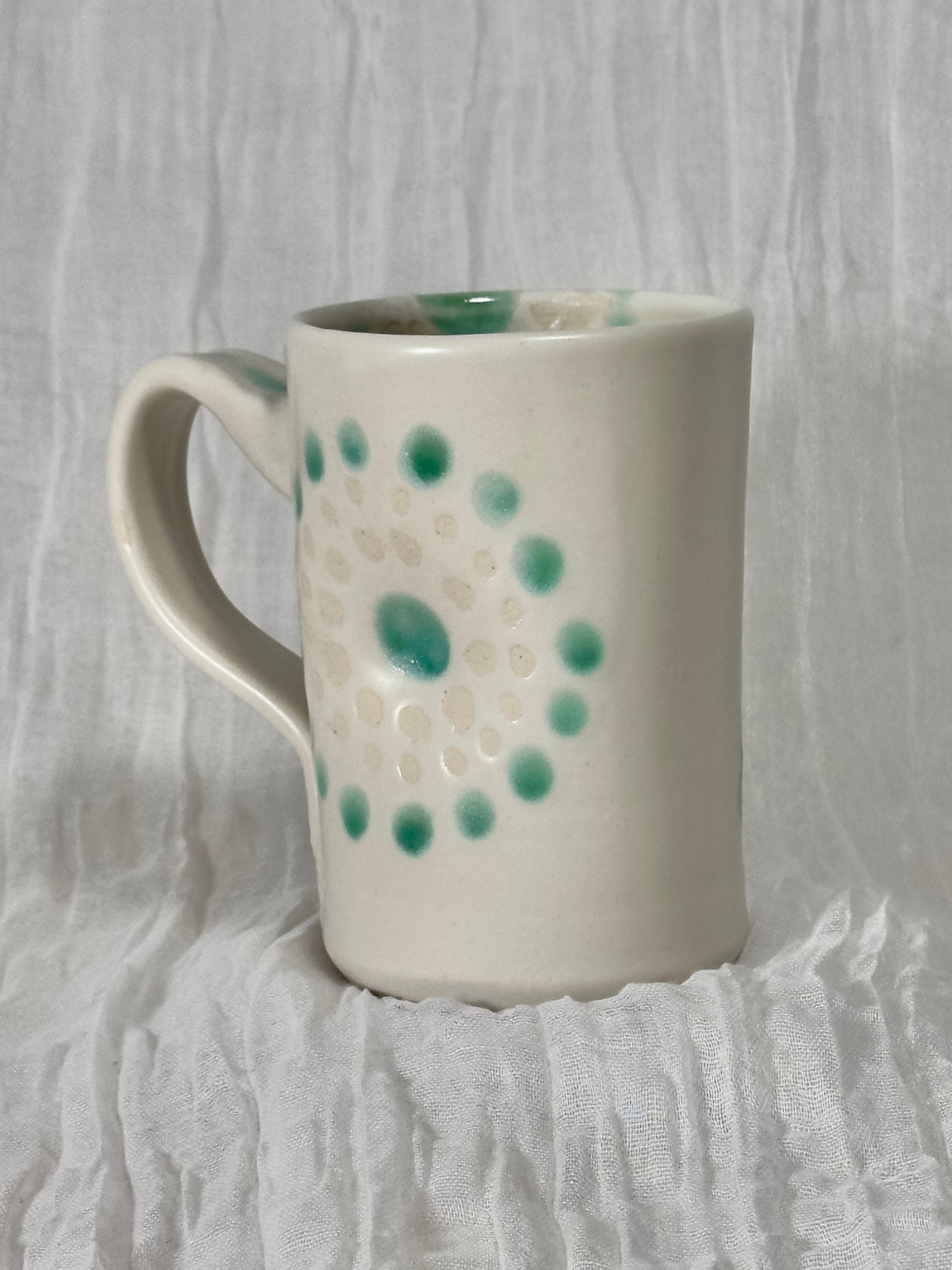 White ceramic mug with green speckles on a textured white background