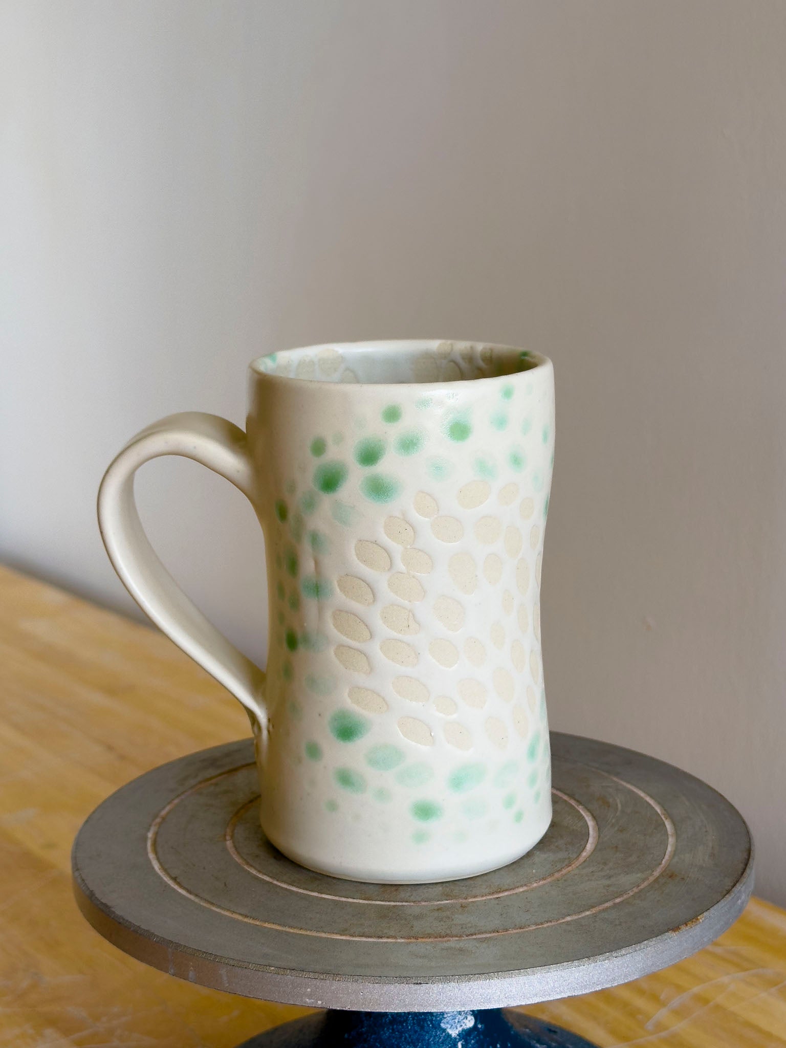 Ceramic mug with green and beige pattern on a wooden surface
