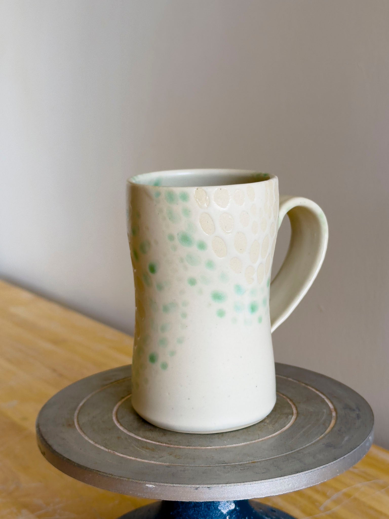 White ceramic mug with green speckles on a wooden surface