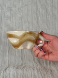 Hand holding a ceramic mug with brown and beige patterns against a textured gray background