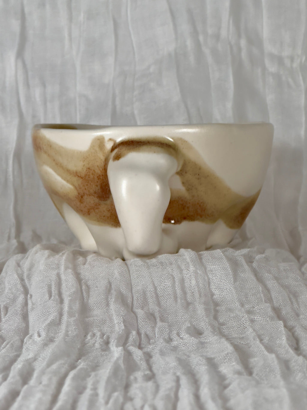 Ceramic bowl with brown and white glaze on a textured white surface
