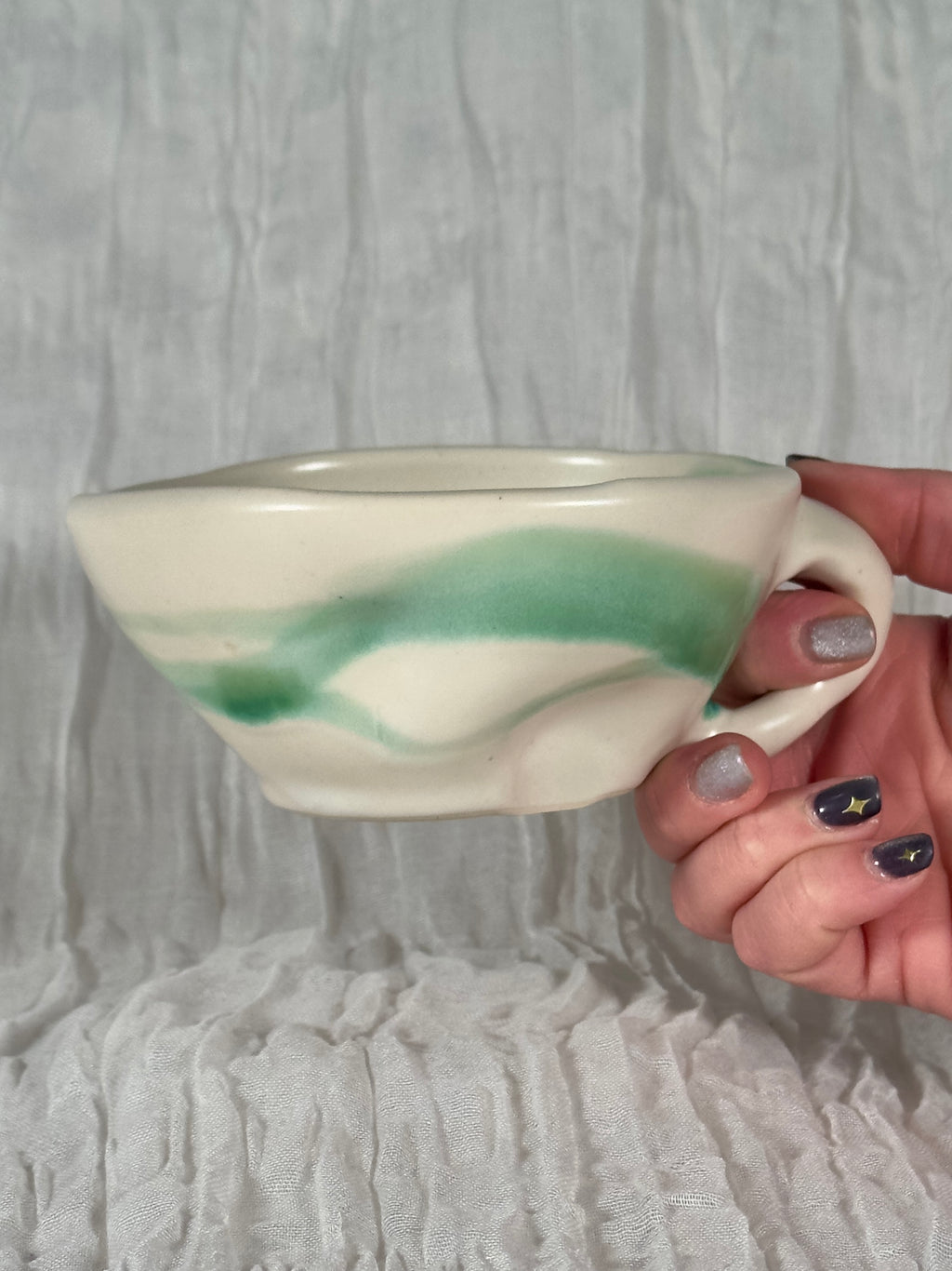Hand holding a ceramic cup with green and white design against a textured gray background