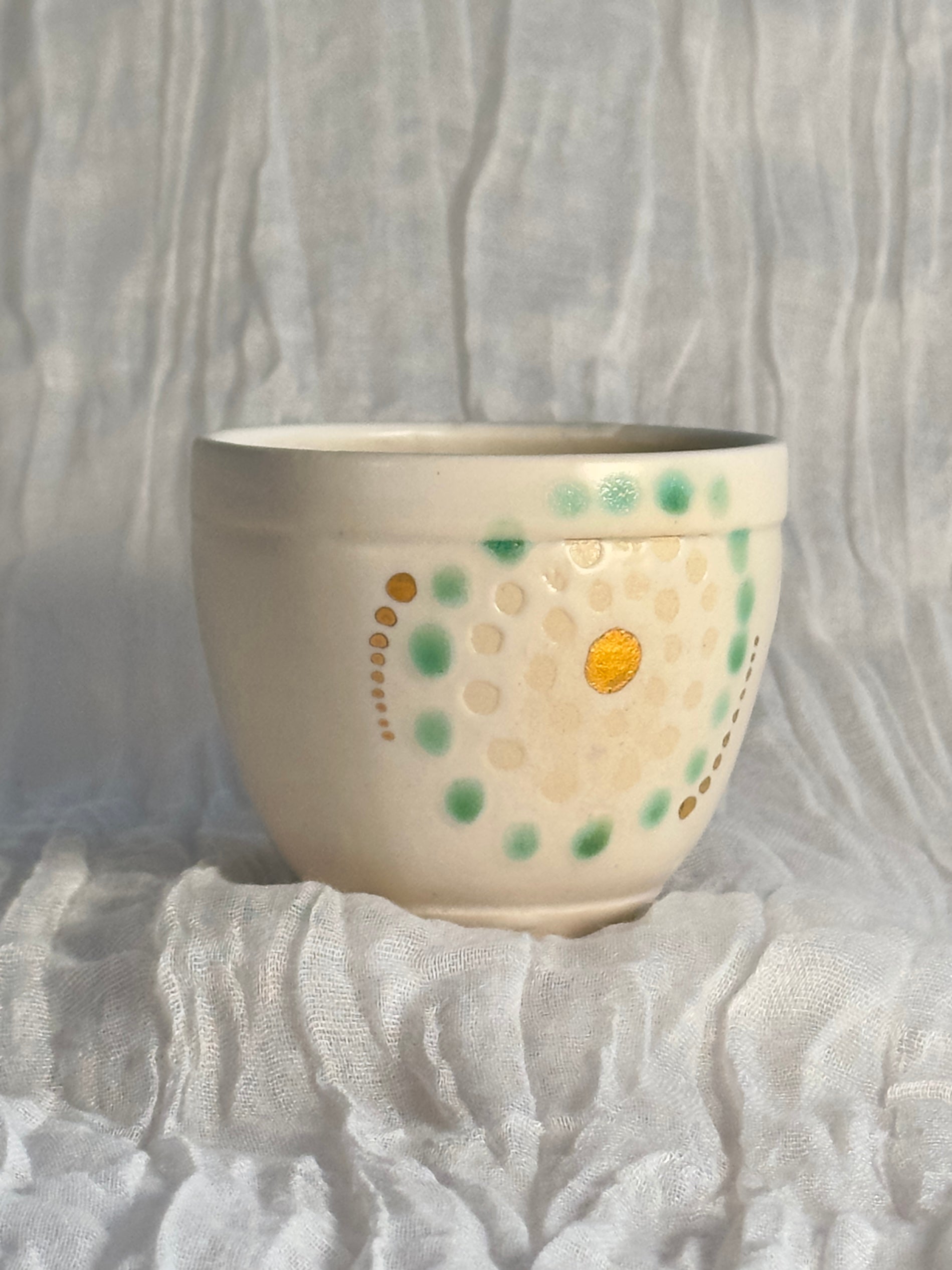 Ceramic bowl with green and gold patterns on a textured white background