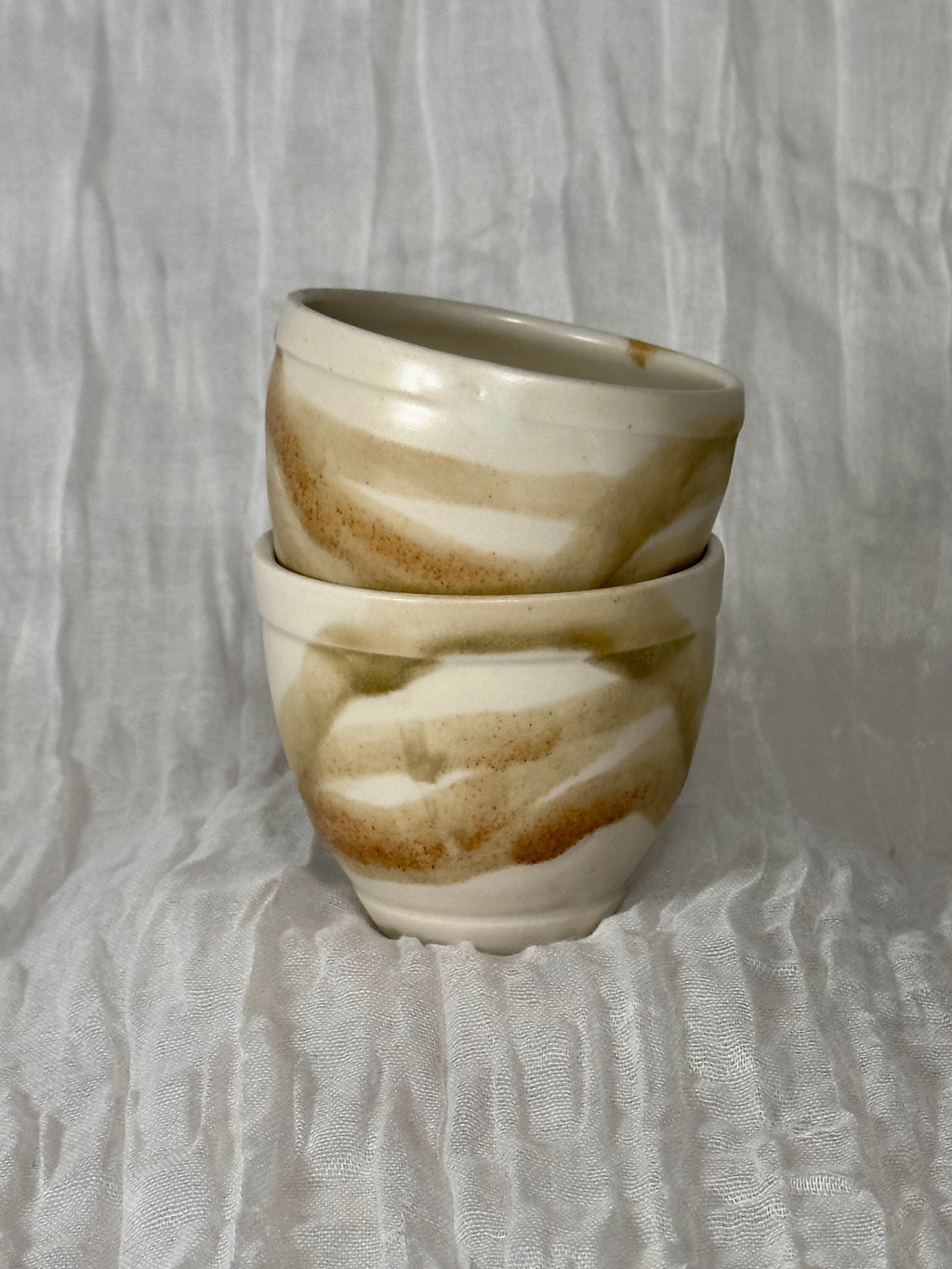 Two stacked ceramic cups with a marbled pattern on a textured gray background